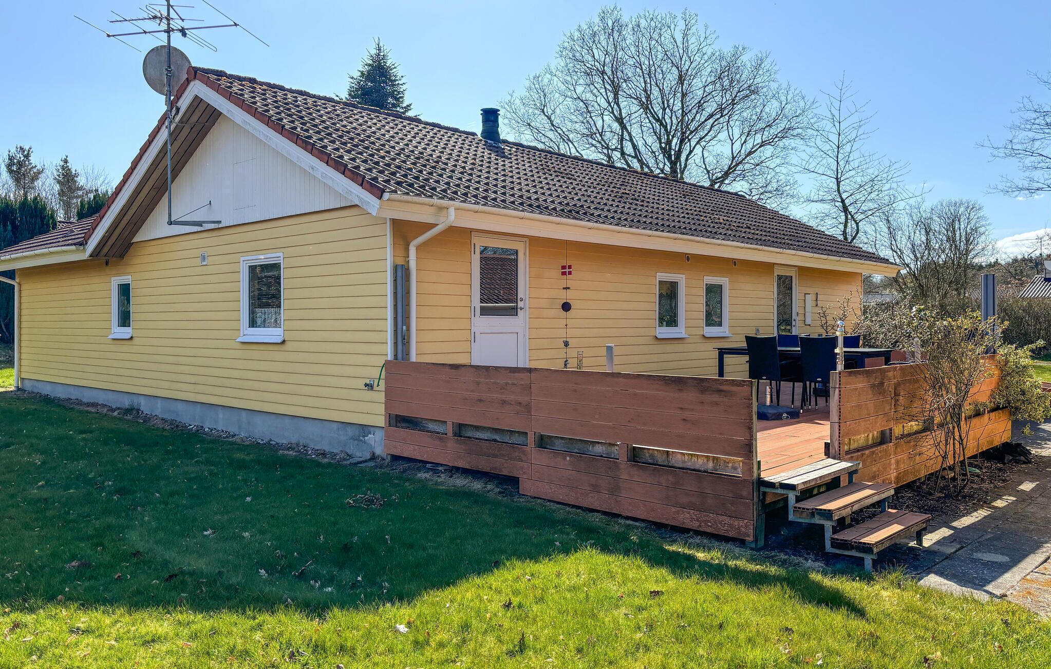 Une maison jaune d’un seul étage, avec un toit en tuiles, un porche à l’avant et une petite terrasse.