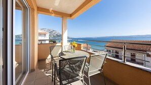 A balcony with a table and chairs, overlooking a coastal view with buildings and a mountain in the distance. - Beautiful apartment in Duce with house sea view (Duce)