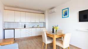 A modern kitchen with white cabinets, a wooden dining table, and chairs. There is a small potted plant on the counter and a vase with flowers on the table. - Beautiful apartment in Duce with house sea view (Duce)