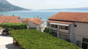 A residential area with terracotta-tiled roofs, a parked car, and a view of a body of water with boats. - Beautiful apartment in Duce with house sea view (Duce)