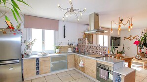 A modern kitchen with a stainless steel refrigerator, a built-in oven, and a dishwasher. There is a large window providing natural light, and the kitchen features a wooden countertop and a hanging light fixture. - Beautiful home in Grospierres (Grospierres)