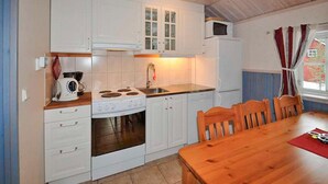 A compact kitchen with white cabinets, a stove, a sink, and a microwave. There is a wooden dining table with chairs. - Nice apartment in Sälen with sauna (Sälen)