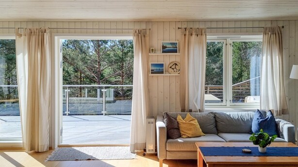 A cozy living room with a grey sofa, a coffee table, and a view of a balcony and trees.