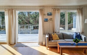 Ein gemütliches Wohnzimmer mit grauem Sofa, einem Couchtisch und Blick auf einen Balkon und Bäume.