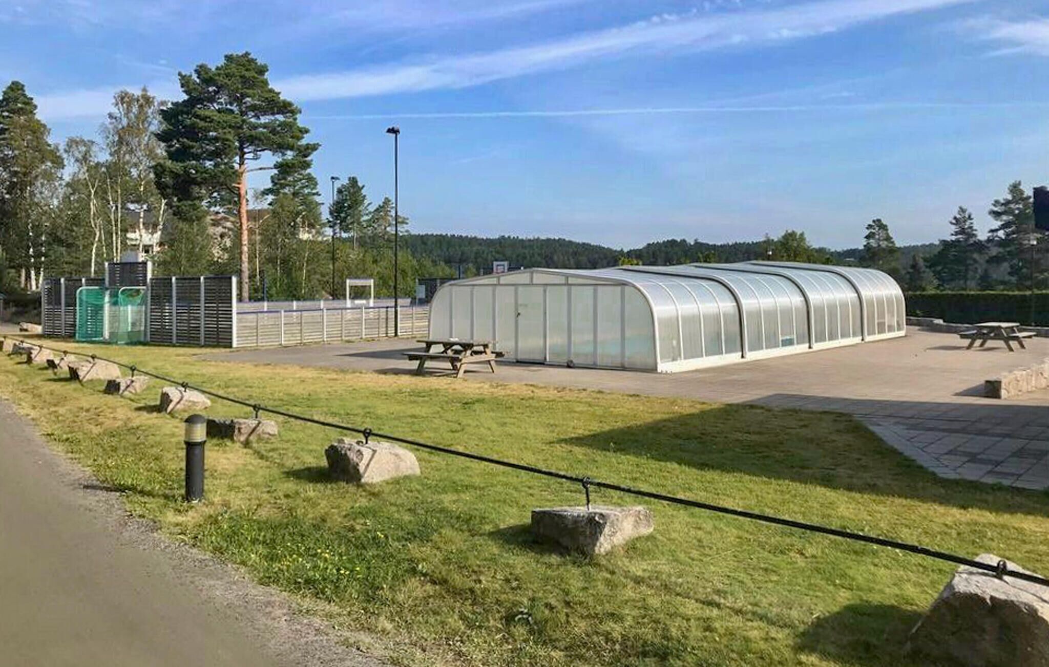 En växthuskonstruktion med ett böjt tak, omgiven av ett stenlagt område med picknickbord.