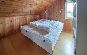 Ett enkelrum med träpanel på väggarna och ett sluttande tak, inrett med ett fönster och en väggmonterad lampa.