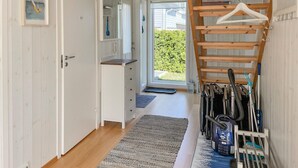 A hallway with a wooden floor, a white door, a small window, and a rack with cleaning tools.