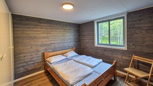 A bedroom with a wooden bed, a window with a view of trees, and a wooden chair.