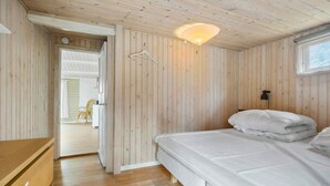 Une chambre aux murs lambrissés, avec un lit, un luminaire suspendu et une vue sur une autre pièce.