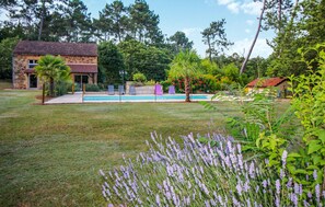 Une maison en pierre avec une piscine, entourée d’une pelouse bien entretenue et de diverses plantes.