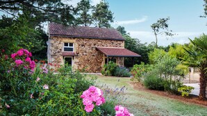 A stone house with a tiled roof, surrounded by lush greenery and flowering plants.