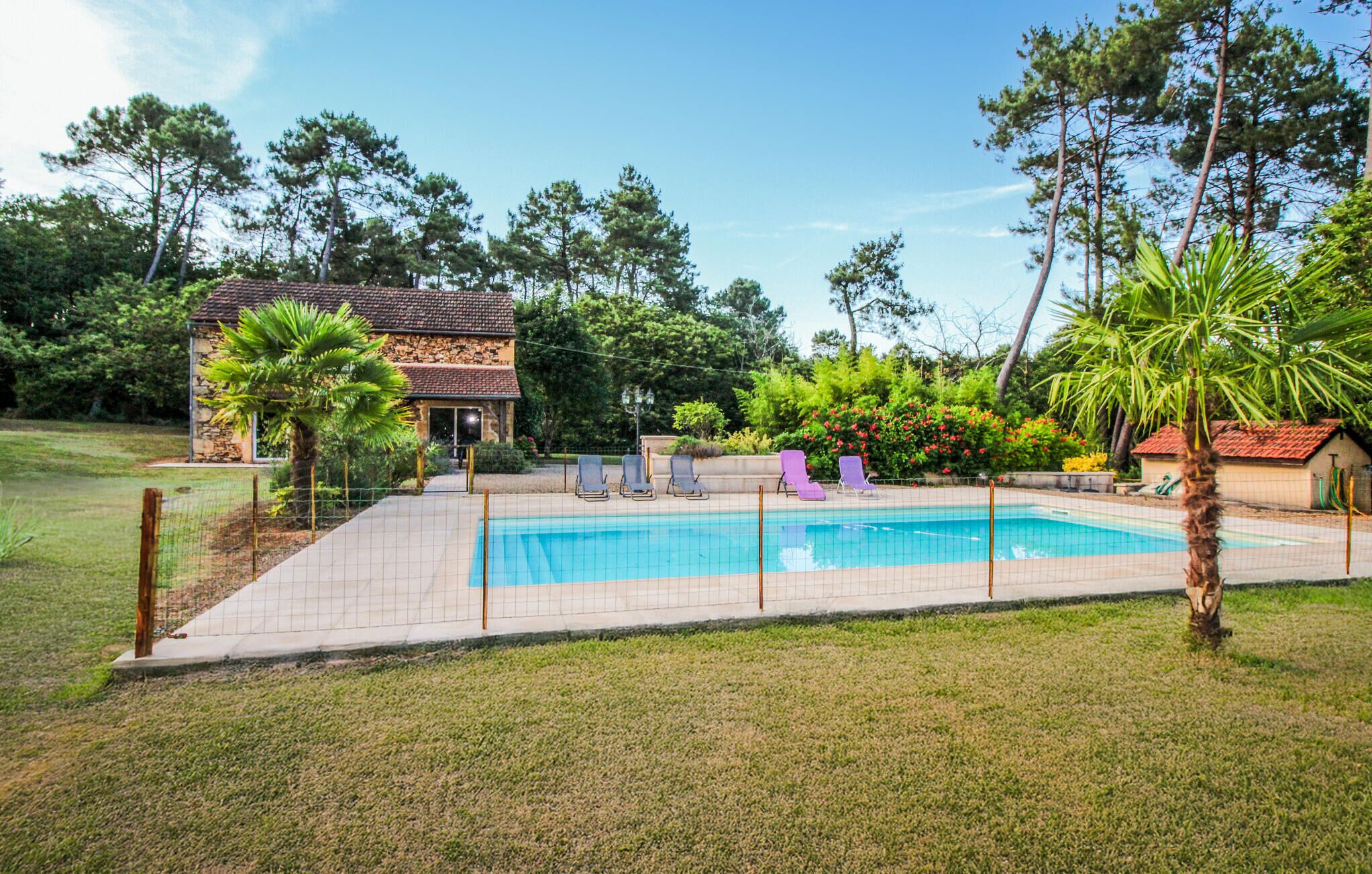 Une piscine entourée de chaises longues, un bâtiment en pierre et une végétation luxuriante.