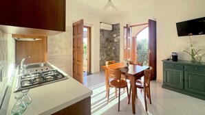 A kitchen with a gas stove, wooden cabinets, a dining table with chairs, and a TV on the wall.