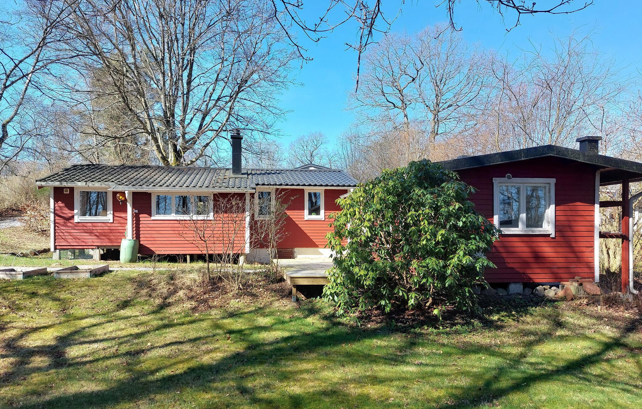 A red cabin with a chimney, a small porch, and a green bush in front.