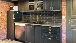 Uma cozinha com armários escuros, painel de azulejos preto, pia de aço inoxidável e micro-ondas na bancada.