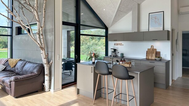 A modern kitchen with a central island, bar stools, and a view of the outdoors. - 3 bedroom amazing home in Nexø (Nexø)