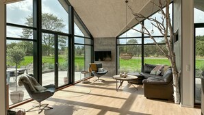 A spacious living room with large windows, a fireplace, and a view of a green landscape. - 3 bedroom amazing home in Nexø (Nexø)