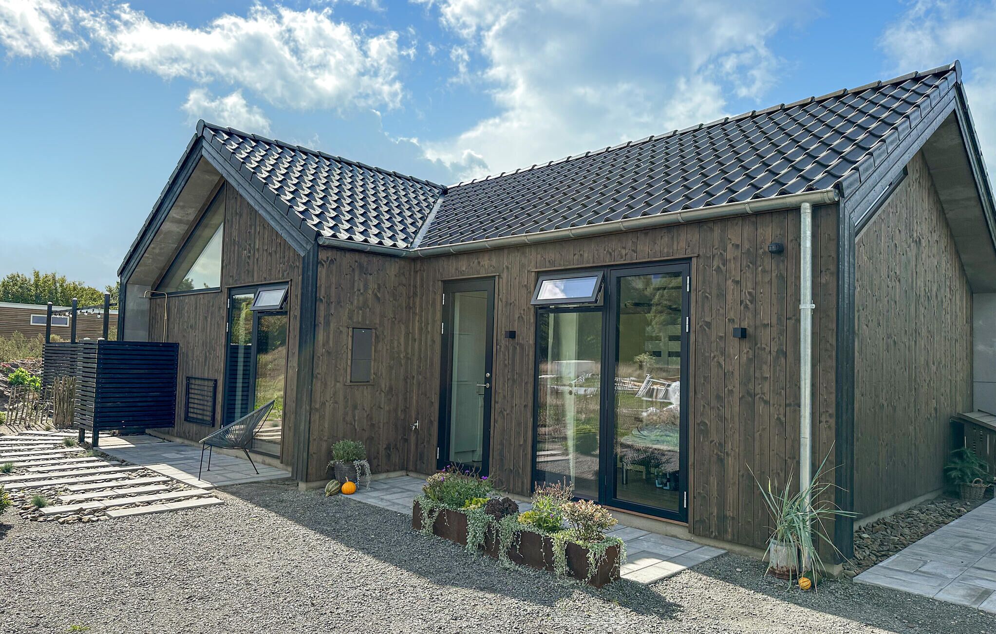 A modern house with a sloped roof, large sliding glass doors, and a gravel driveway.