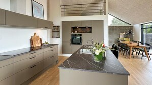 A modern kitchen with a central island, wooden cabinets, and a dining area with a wooden table and chairs. - 3 bedroom amazing home in Nexø (Nexø)