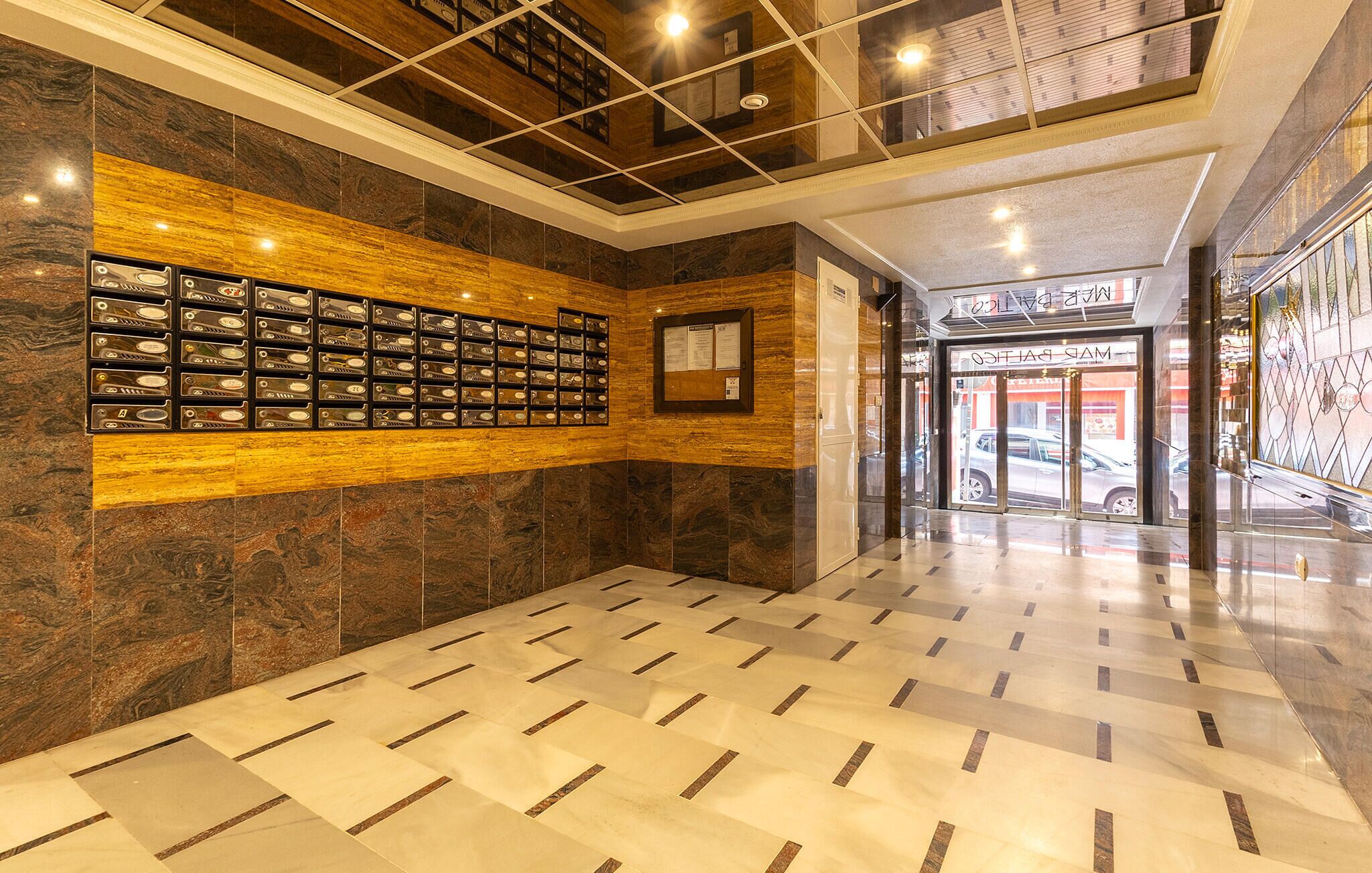 A lobby with a patterned floor, a wall-mounted display of various items, and a door leading to a shop.
