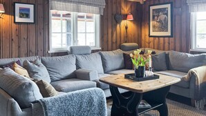 A cozy living room with a grey sectional sofa, a wooden coffee table, and a small side table with a candle and flowers. - Cozy home in Nissedal with sauna (Nissedal)