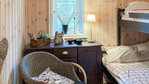 A cozy room with a wooden interior, a window with a view, a desk with a lamp, a wicker chair, and a bed with a patterned bedspread. - Cozy home in Nissedal with sauna (Nissedal)