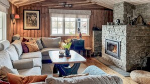 A cozy living room with a stone fireplace, wooden walls, a sofa, and a coffee table. - Cozy home in Nissedal with sauna (Nissedal)