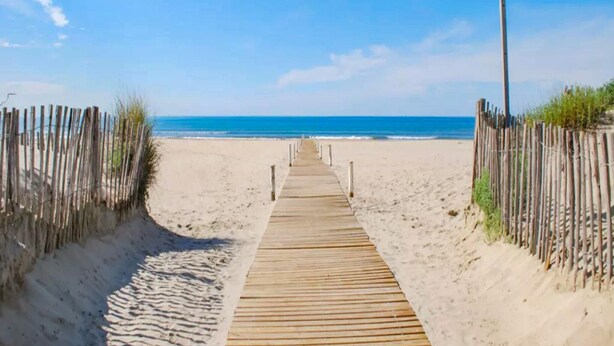 Une promenade en bois qui mène à une plage, avec un ciel dégagé.