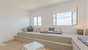 Un salon moderne doté d’un banc intégré, d’une table blanche et d’une grande fenêtre laissant entrer la lumière naturelle.