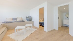 Une chambre à coucher moderne avec un lit, une table de chevet et une chaise. On aperçoit une salle de bain avec un miroir et un lavabo.
