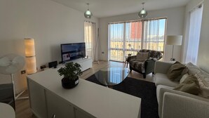 A modern living room with a flat-screen TV, a glass coffee table, a sofa, and a dining table. -  2-bedroom apartment near Canning Town Station E16 1GW London (London)