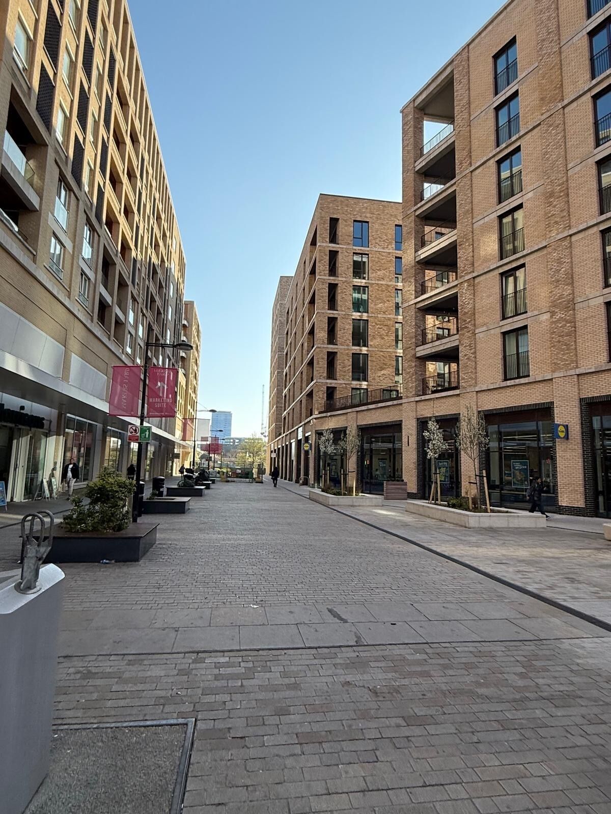 A modern urban street with multi-story buildings, a pedestrian walkway, and storefronts.