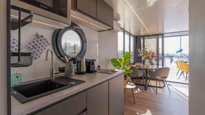A modern kitchen with a sink, kettle, and kettle stand. There is a round mirror above the sink and a window with a view of boats.