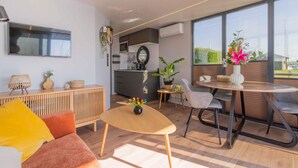 A modern living space with a sofa, a coffee table, a dining table with chairs, a kitchen area, and large windows offering a view.