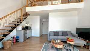 A spacious living area with a staircase, a sofa, a coffee table, and a kitchen area.