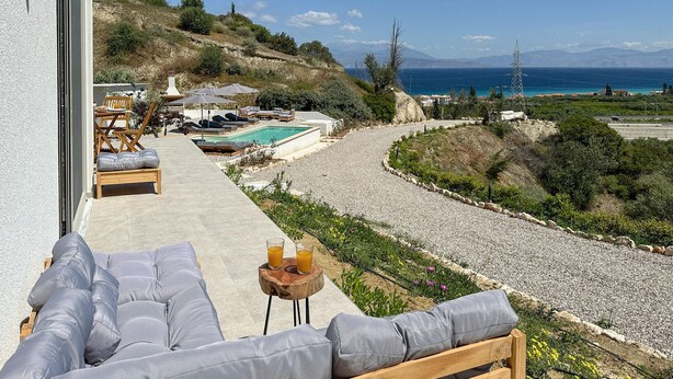A terrace with outdoor seating, a pool, and a view of the sea and mountains.