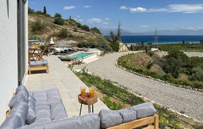 Eine Terrasse mit Sitzgelegenheit im Freien, einem Pool und Blick auf das Meer und die Berge.