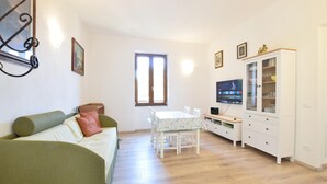 Un soggiorno con un divano verde, un tavolo da pranzo con sedie, una televisione e un mobile contenitore con ante in vetro.