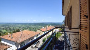 Un balcone con ringhiera metallica che si affaccia su una città con tetti in tegole rossastre e un cielo azzurro intenso.