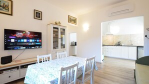 Un soggiorno con televisore, tavolo da pranzo e sedie. È presente un angolo cottura con pensili e lavello.