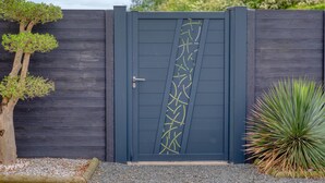 A dark wooden gate with a decorative pattern, a small tree, and a plant beside it. - 2 bedroom amazing home in Créances (Créances)