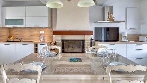 A modern kitchen with white cabinetry, a central island with seating, a fireplace, and overhead pendant lighting. - 2 bedroom amazing home in Créances (Créances)