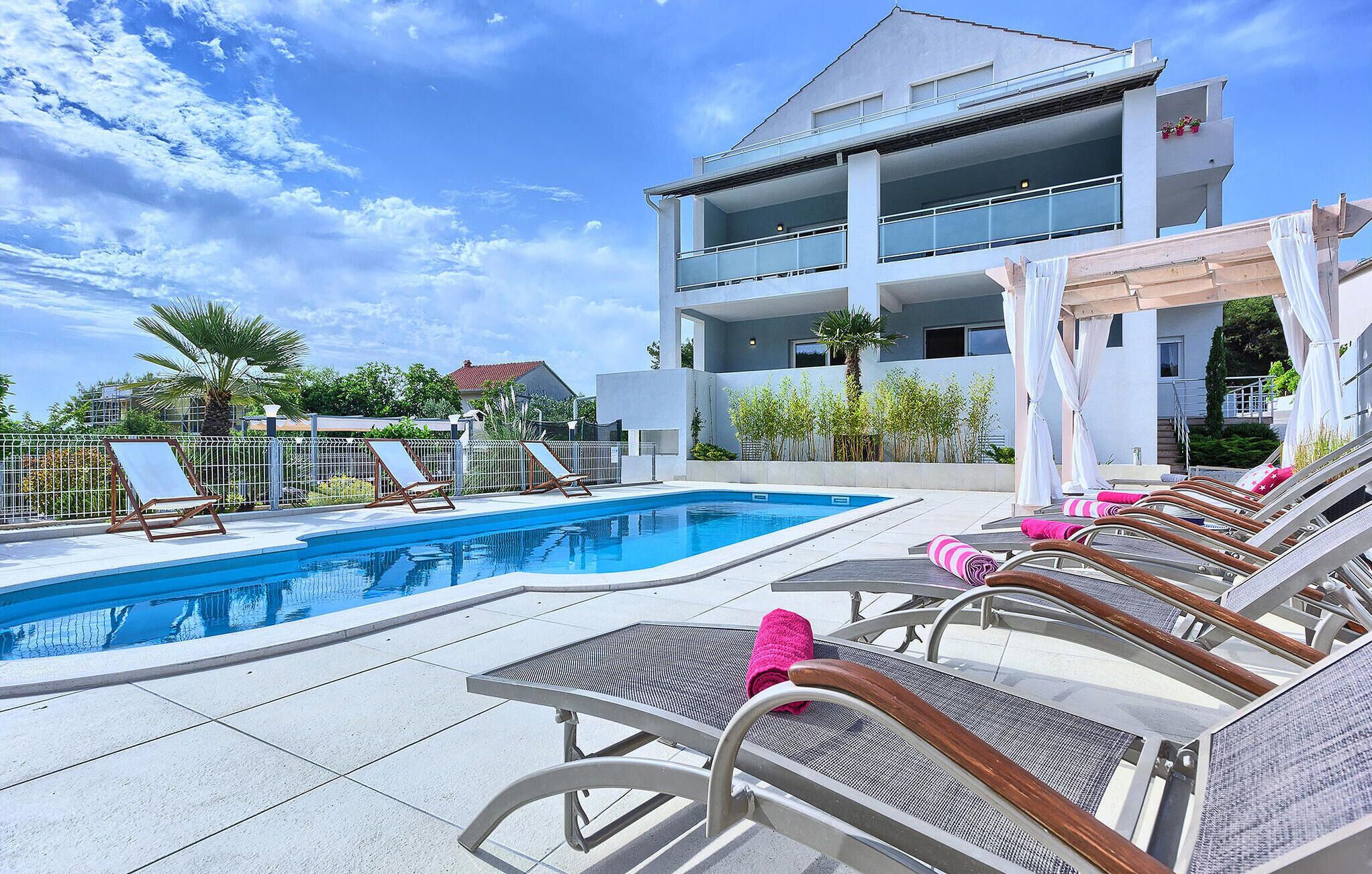 Un hôtel moderne doté d’une piscine, de chaises longues et d’un bâtiment à deux étages avec des balcons.