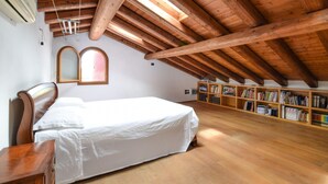 A bedroom with a wooden ceiling, a bed, a nightstand, a bookshelf, and a window. - Cozy home in Rosà with WiFi (Rosà)