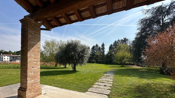 A covered patio area with a brick column, a stone pathway, and a grassy lawn with trees. - Cozy home in Rosà with WiFi (Rosà)