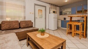 A compact living space with a sofa, a wooden table, a refrigerator, and a kitchen area with cabinets and a microwave.