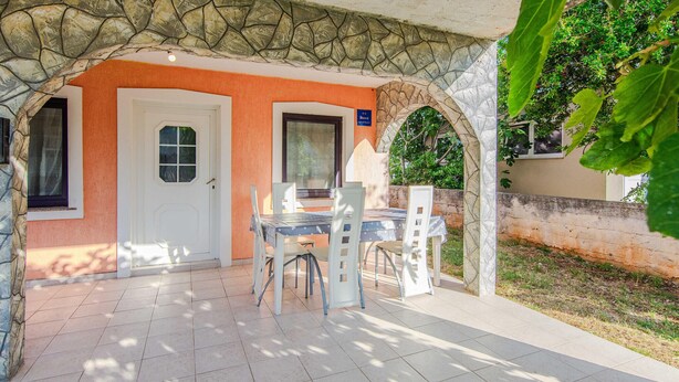 An outdoor patio with a stone archway, a white door, and a table with chairs.