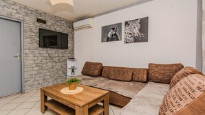 A living room with a stone wall, a flat-screen TV, a wooden coffee table with a plant, a brown sofa with patterned cushions, and two framed animal paintings.