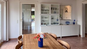 A dining area with a wooden table, chairs, a blue vase with flowers, and a white cabinet with glass doors displaying various items. - Lovely home in Kirke Hyllinge (Kirke Hyllinge)