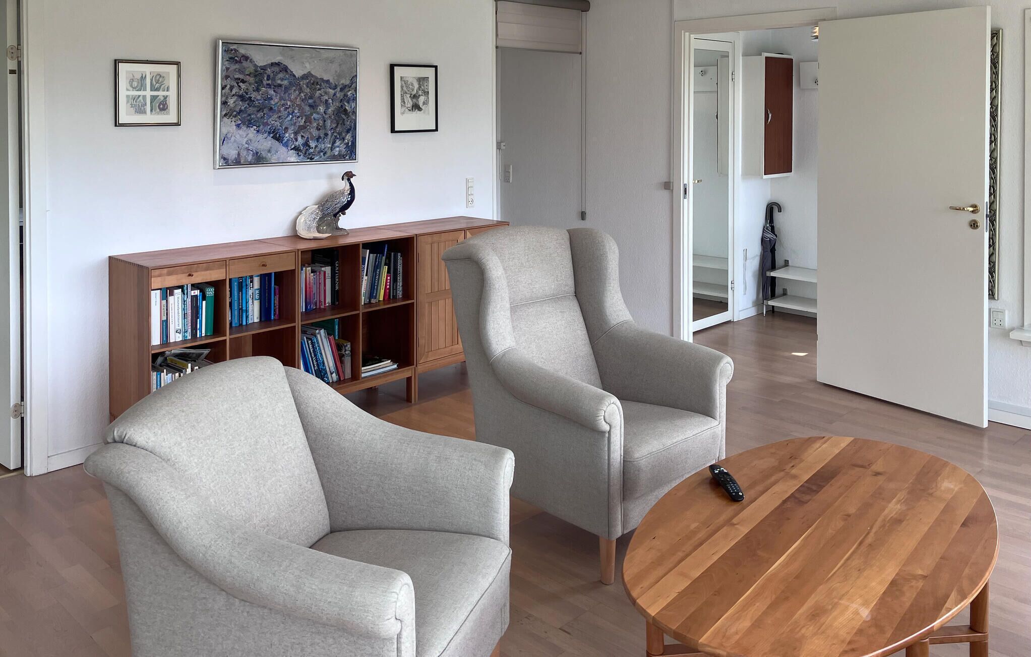 Una sala de estar con dos sillones grises, una mesa de centro de madera y una estantería llena de libros.